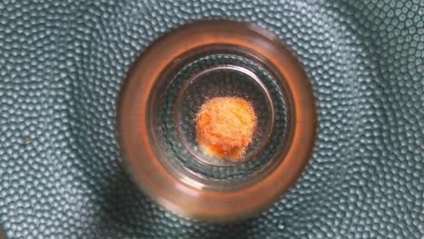 vista de ángulo alto de una tableta efervescente naranja disolviéndose en el fondo de un vaso de agua