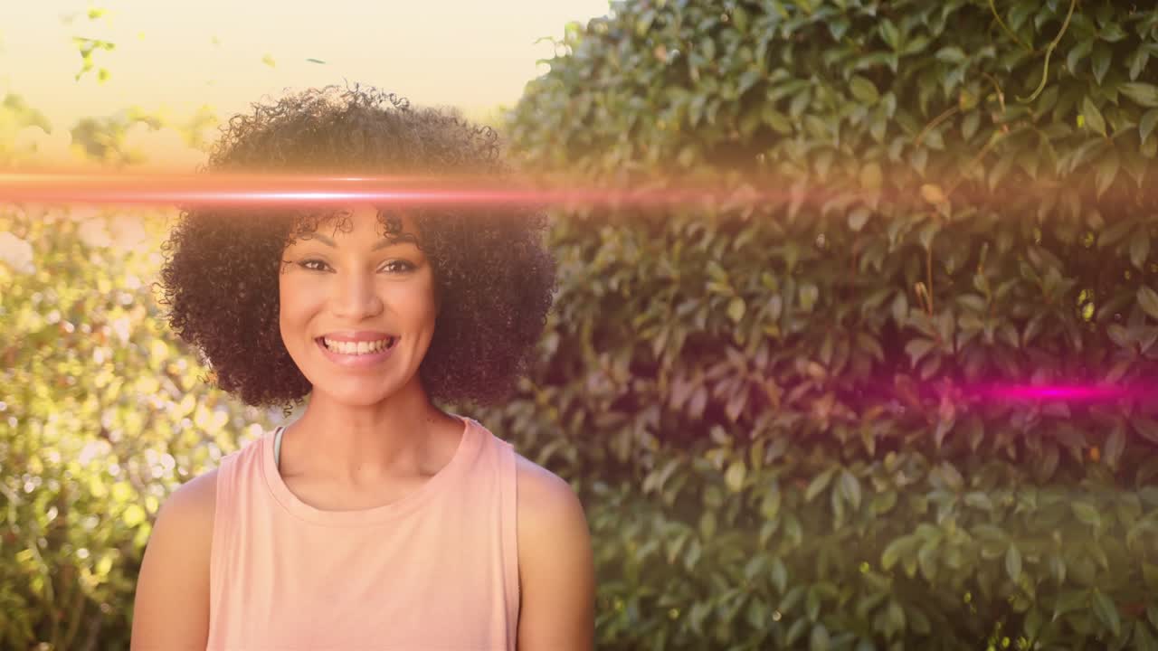 Woman modeling fashion ad by hedge, lens flare sweeping across face causing smiling, light shifting