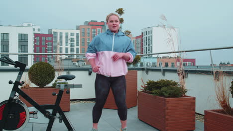 sport fit woman in sportswear exercise kicking, punching, high leg kick on roof of house, aerobic