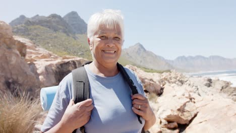 portrait of happy senior biracial woman in mountains with backpack, in slow motion