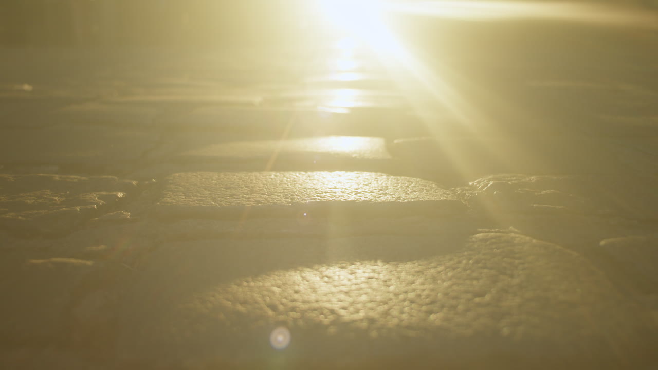 La superficie mojada de la calle adoquinada refleja la cálida luz del atardecer mientras la gente pasa.