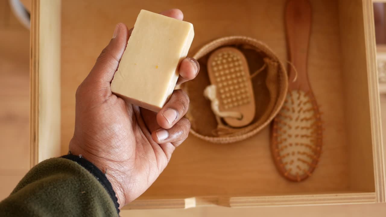Hand holding soap bar in wooden drawer with other natural care products