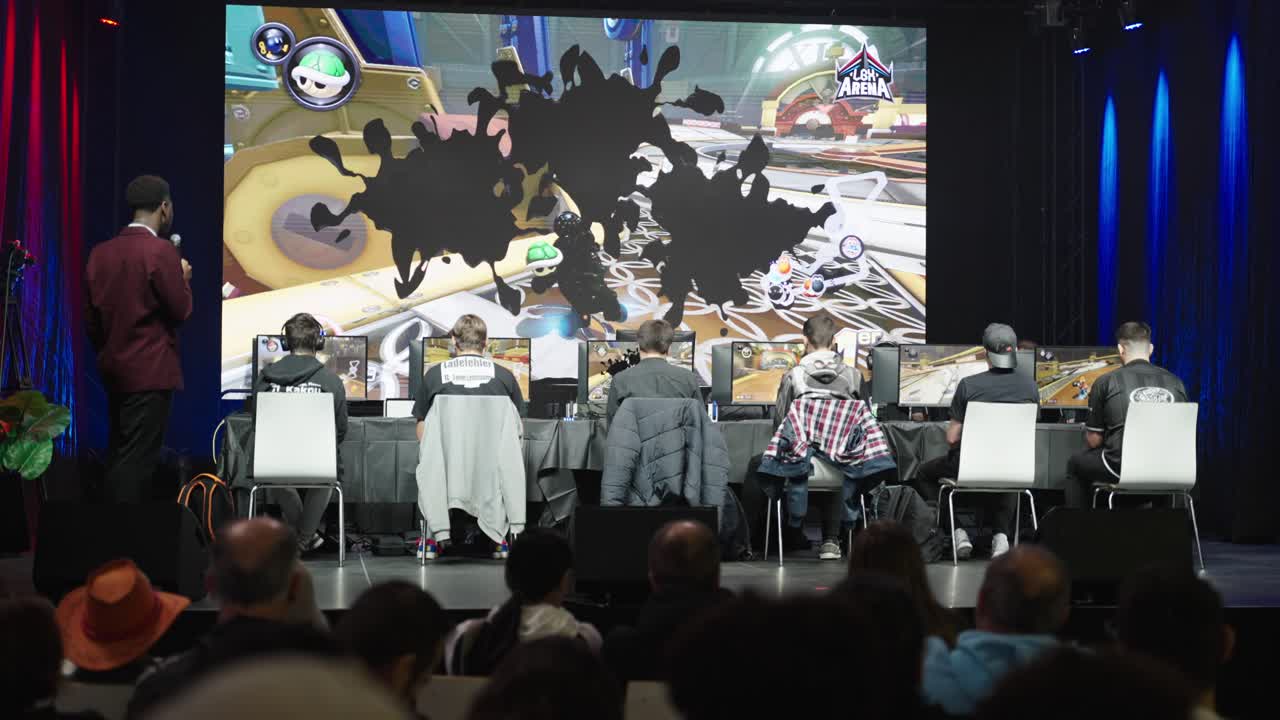 Kids on stage at a Mario Kart Tournament finals in front of the crowd watching them racing at a convention Event while a speaker commenting the game at LGX Luxembourg