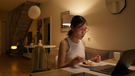 Woman Eating Sushi While Working on Laptop at Night