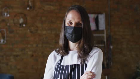 smiling caucasian female business owner with crossed hands, wearing face mask and apron