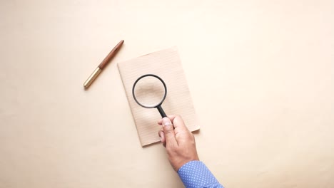 person using magnifying glass to inspect notebook