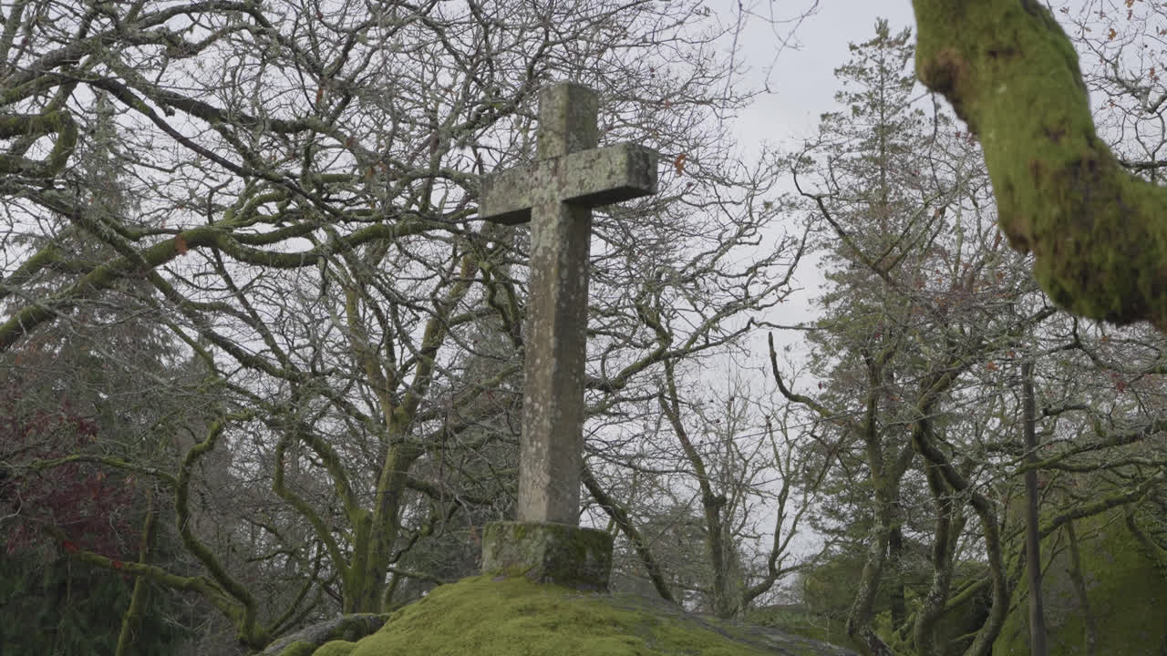 Close view of stone cross on small hill surrounded by bare forest trees
