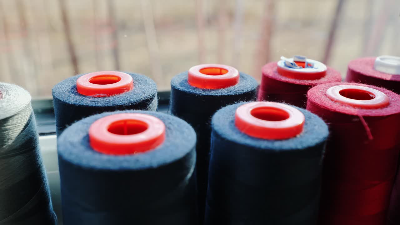 Close up textile spools in dark tones with red centers illuminated, window light
