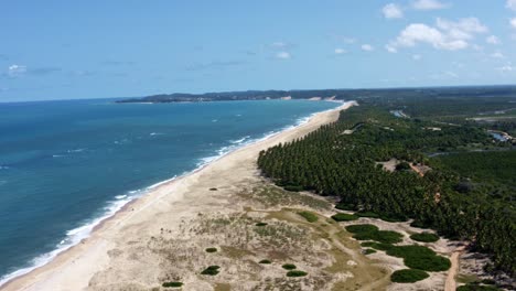 Trucking-left-aerial-drone-wide-shot-of-the-tropical-coastline-of-Rio-Grande-do-Norte,-Brazil-with-a-white-untouched-beach,-blue-ocean-water,-and-palm-trees-in-between-Baia-Formosa-and-Barra-de-Cunha?