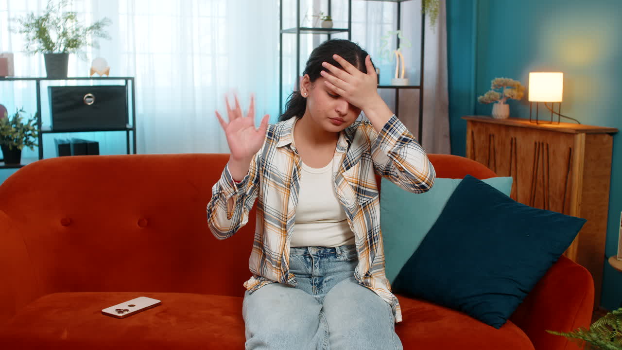 Indian woman sadly looking at smartphone doing facepalm covering face feeling defeated frustrated