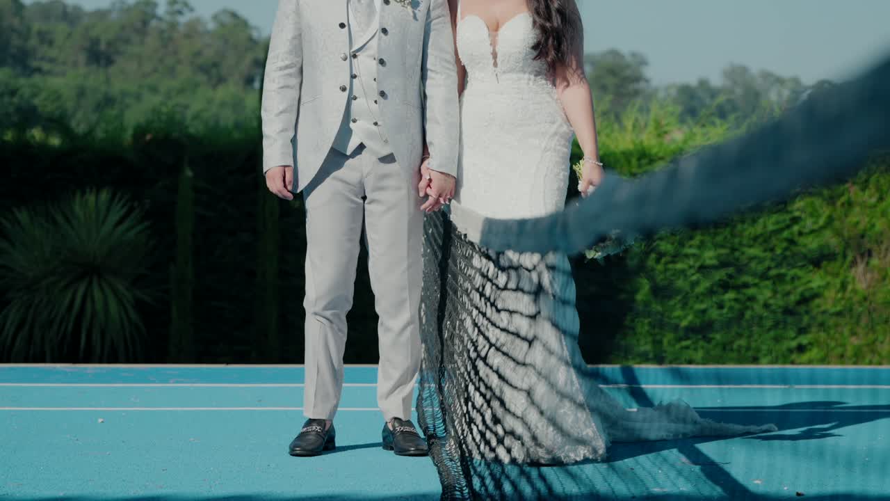 신랑과 신부는 손을 잡고 파란 테니스 코트를 고 있습니다.