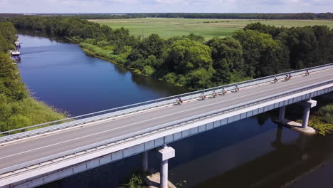 a group of bikers cross a bridge over a river in the lithuanian countryside