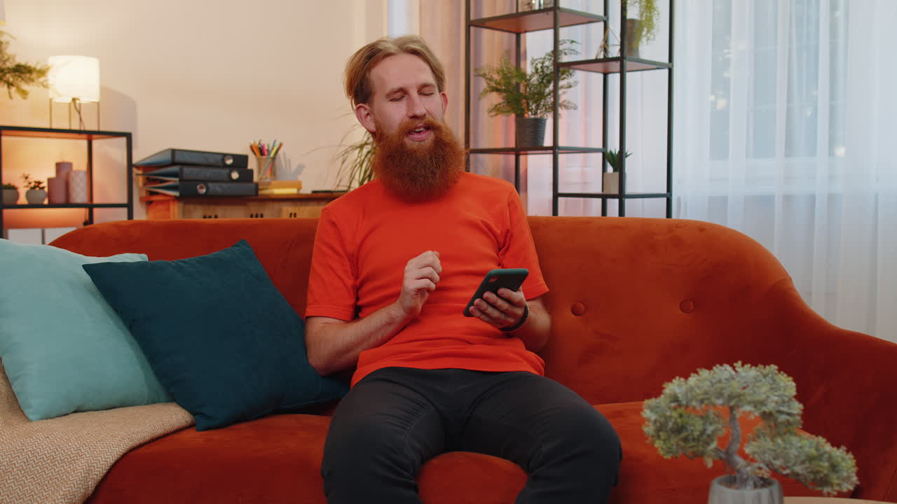 Portræt af en voksen mand, der sidder i sofaen og bruger sin smartphone til at dele beskeder på sociale medier