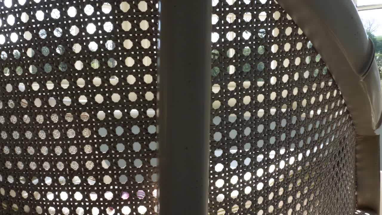 창가 옆에 있는 빈 흰색 고리버들 의자를 가로질러 천천히 미끄러집니다.