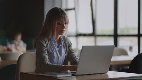 retrato de una joven asiática sentada en una mesa con una computadora portátil y escribiendo en un teclado