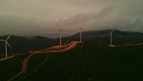 Luftaufnahme-Eines-Windparks-Zur-Erzeugung-Erneuerbarer-Energie-In-Form-Von-Strom-Und-Energie-Für-Die-Bevölkerung-Zum-Optimalen-Umweltschutz-Mit-Blick-Auf-Die-Berge-An-Einem-Sommerabend