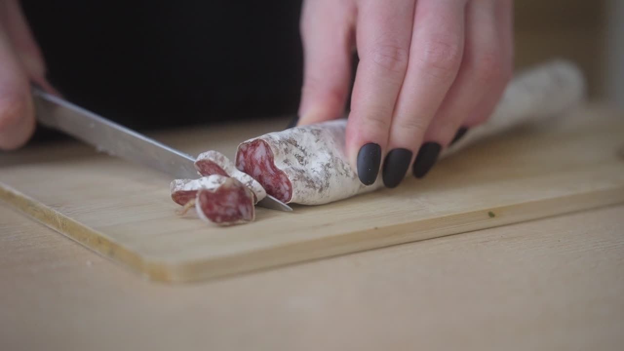 Slicing fuet salami into thin slices using a knife. Preparing a delicacy at home. Closeup shot