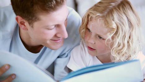 child reading a book aloud with his father