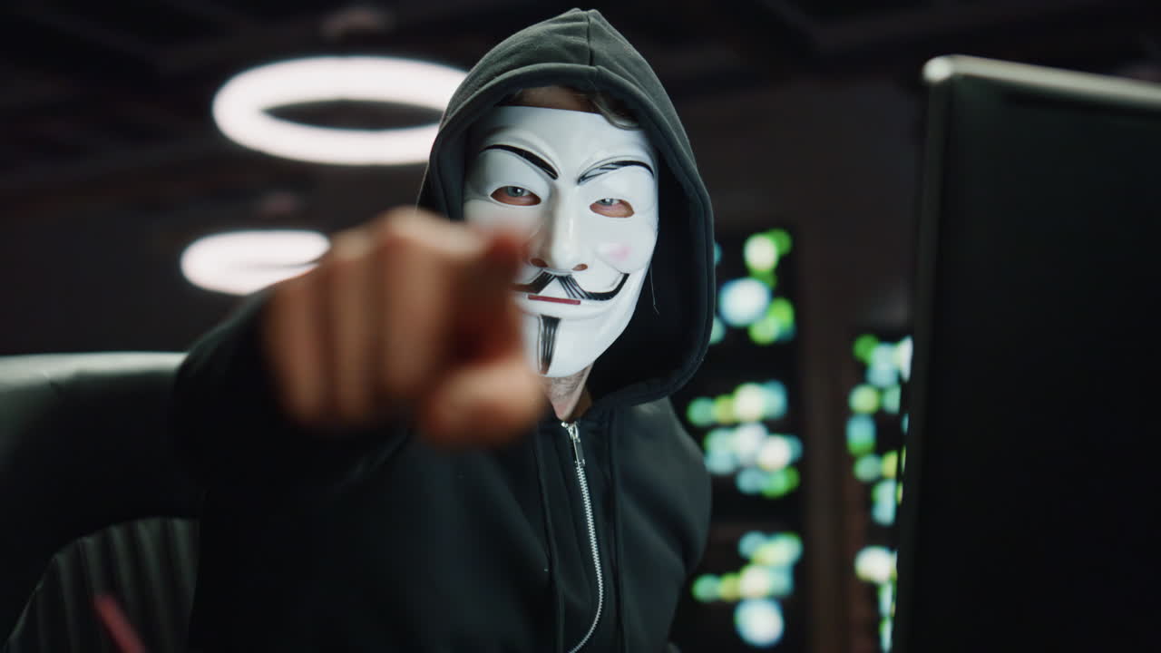 hacker encapuchado rompiendo servidores de datos de cerca por la noche. hombre enmascarado señalando con el dedo