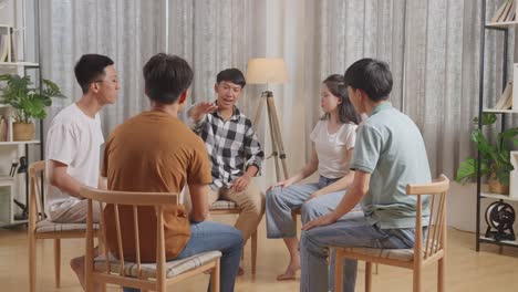 아시안 십대 그룹은 의자에 앉아서 집에서 토론하는 원을 형성합니다. 팀워크의 상징으로 손을 함께 넣고, 비명을 지르며 축하합니다.
