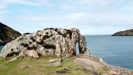 aerial view rising orbit across scenic rock archway on the welsh coastline with calm blue ocean