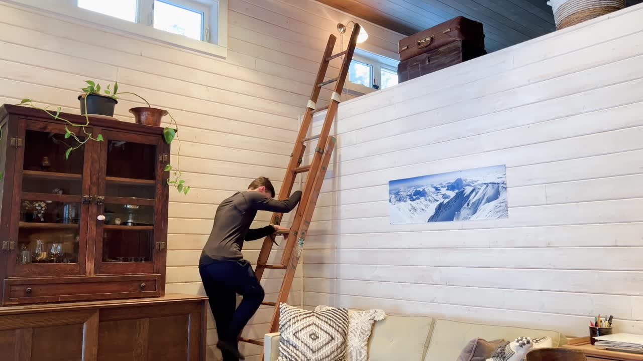 Man climbing up a wooden ladder into the top loft of a ski cabin in Revelstoke British Columbia