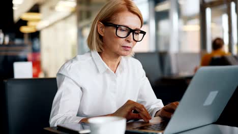 corporate manager mature lady working with laptop in cafe typing business e-mail