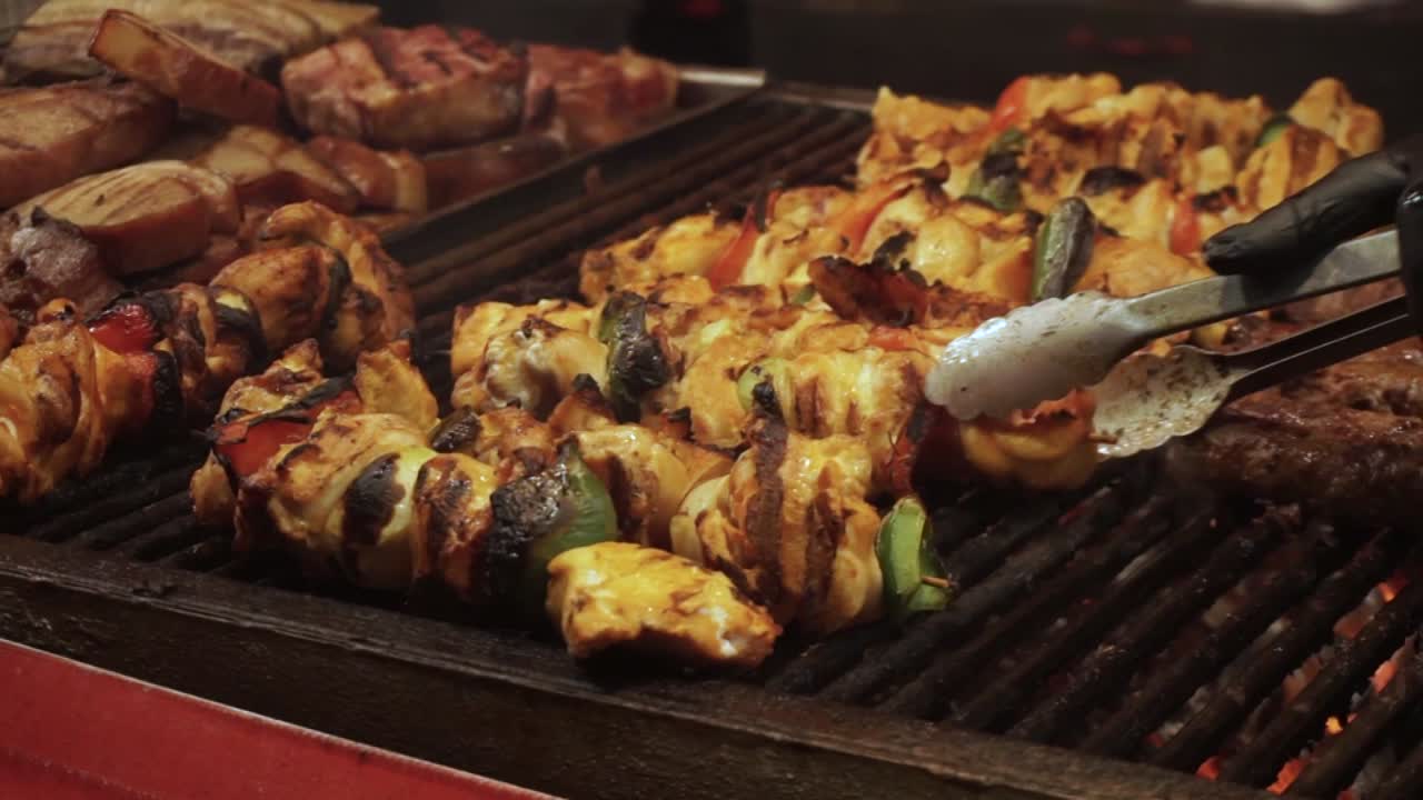 Pollo ruspante biologico alimentato a mais con verdure su spiedini, cotto su una griglia a legna e carbone all'aperto durante un festival tradizionale della carne, ripresa ravvicinata dello chef che gira la carne sulla griglia