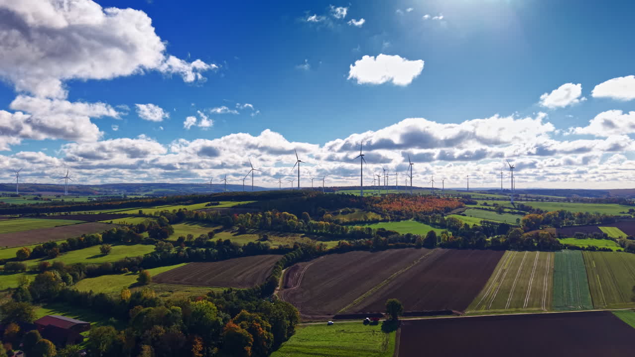 Verdi campi lussureggianti si estendono sulle dolci colline sotto un cielo azzurro e limpido, punteggiato da nuvole soffici e turbine eoliche che ruotano dolcemente nella brezza.