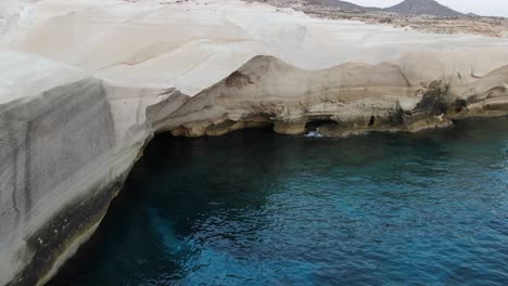 drone view in greece flying over a moon shaped white rock area in milos island at sunrise next to the dark blue sea