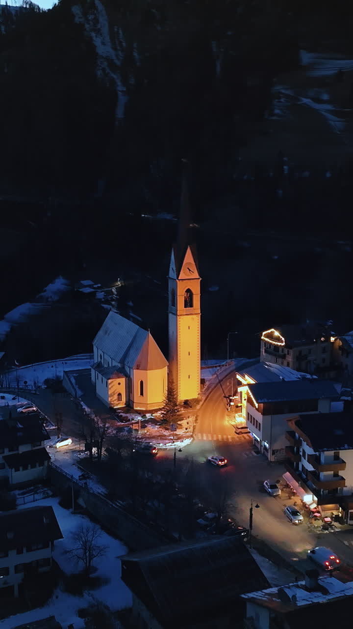 Luftaufnahme mit einer Drohne von der nachts beleuchteten Kirche San Lorenzo in der Gemeinde Selva di Cadore in den Dolomiten, Italien. Vertikal