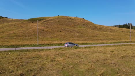 4k drone footage chase car parallel side on an empty road beside a hill