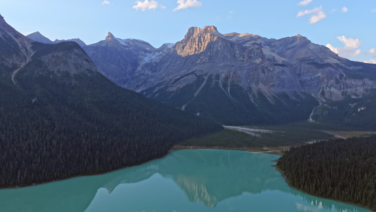 Ripresa cinematografica che rivela un bellissimo lago color smeraldo, circondato da alberi alti e montagne
