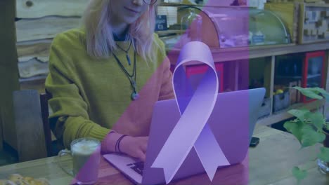 Animation-of-blue-cancer-ribbon-over-caucasian-businesswoman-using-laptop