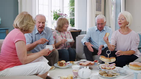 group of senior friends enjoying afternoon tea at home together