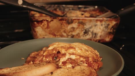 focus pull from lasagna cooking dish to plated meal with garlic bread