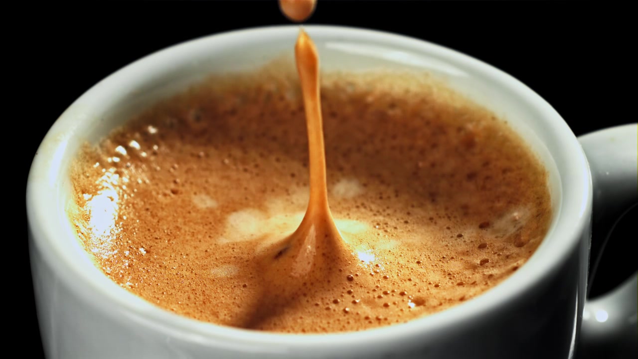 Goccia di caffè al rallentatore che schizza in una tazzina di espresso bianca