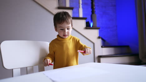 charming baby in yellow sweater comes up to a desk holding a pen. child moves the pen by the paper and sneezes funnily.