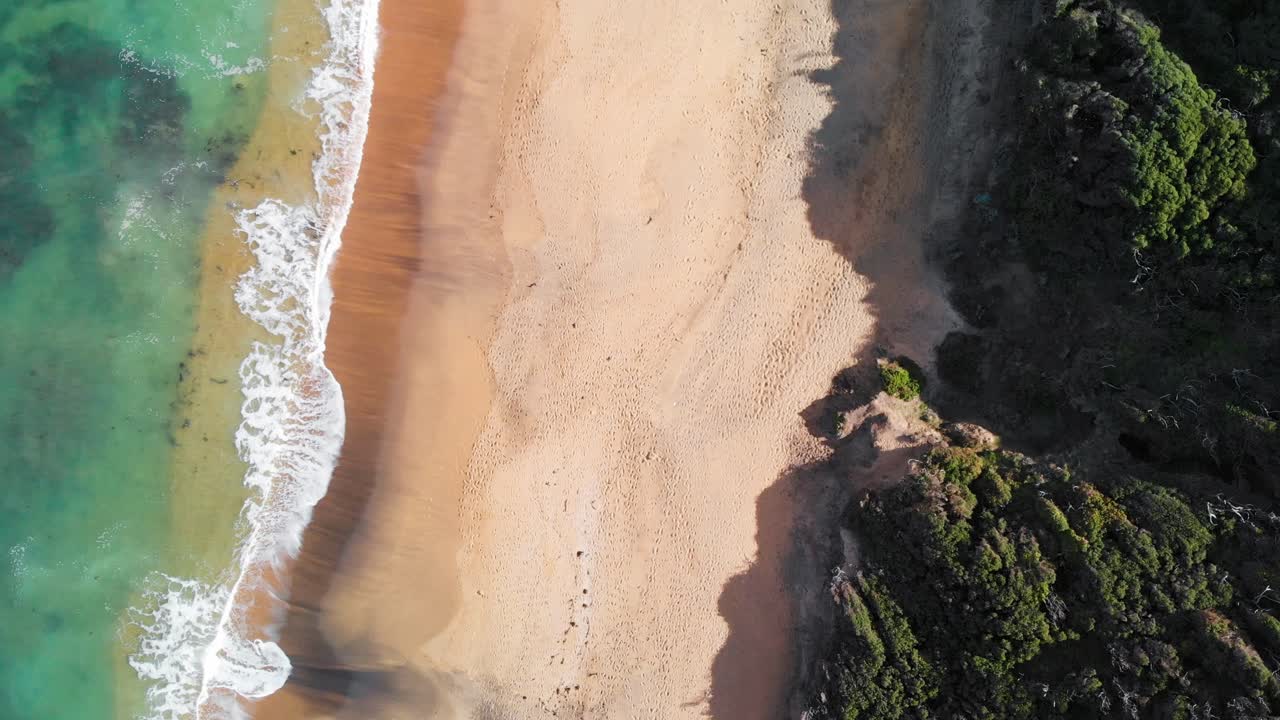 Panoramica mozzafiato a volo d'uccello delle potenti onde che si infrangono sulla incontaminata Bells Beach, Australia, catturata da una ripresa fluida con drone dall'alto