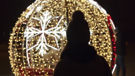 woman standing against large and bright christmas bauble decoration at night