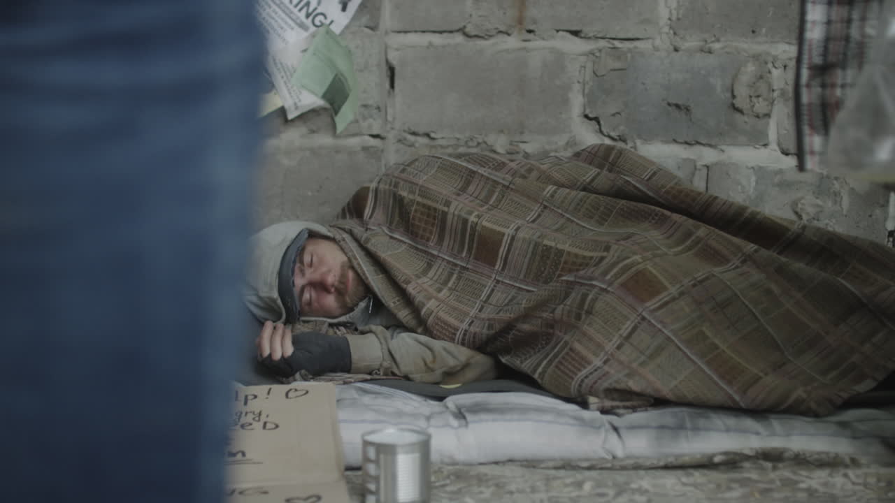 Homeless Person Sleeping on the Street with a Sign for Help