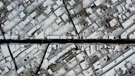 Drone-shot-of-the-city-of-Skardu-from-above,-snow-covered-and-a-road-with-cars