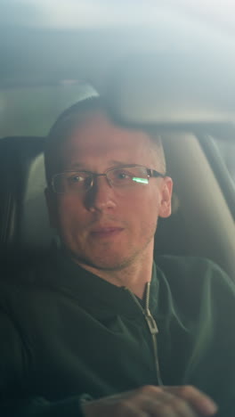 a man is seated in the driver's seat of a car, wearing a green jacket and glasses, gently dancing to music