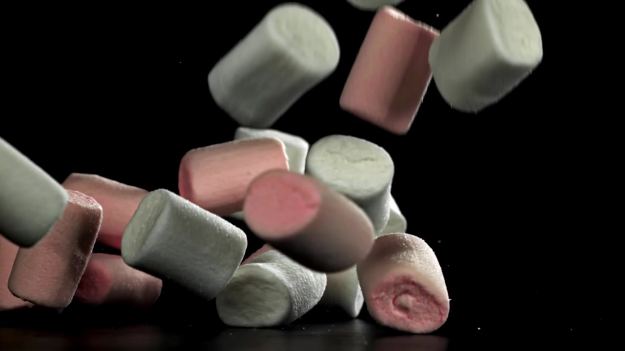 Marshmallow rosa e bianchi che cadono al rallentatore su sfondo nero.