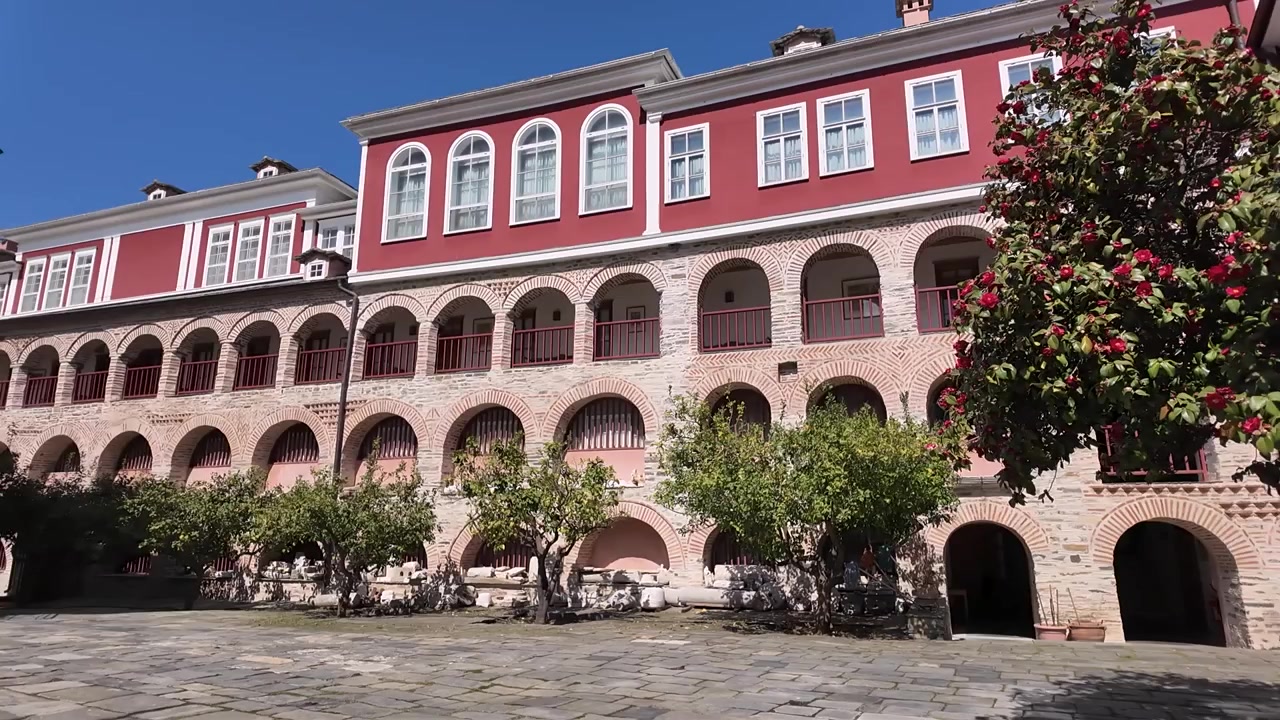 Questo luogo presenta un edificio storico con molti archi. Alberi in fiore circondano il cortile. Un cielo azzurro e limpido contribuisce alle scene luminose. La gente si raduna e si gode il bel tempo.