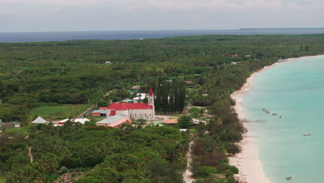 close aerial of saint joseph church on ouvea, new caledonia, showing red roof, tower and tropical greenery set above the lagoon coast