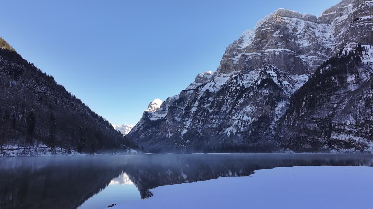Snow-covered mountains reflected in Klöntalersee lake, tranquil winter scene in Glarus