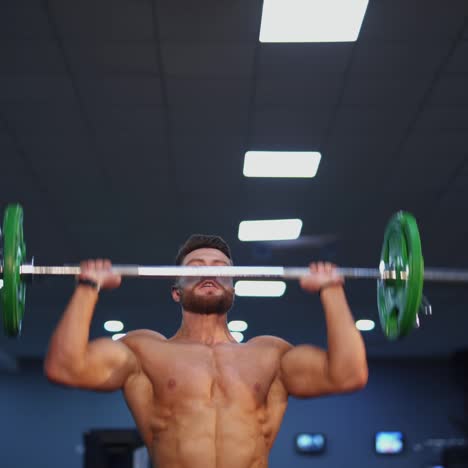 muscular male doing exercises with a bar staying in the gym. athlete lifting barbell up to build his sportive muscles. sportive lifestyle