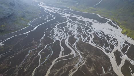 aerial top down shot of braided glacial rivers between volcano mountains during cloudy day in iceland