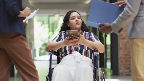 smiling diverse business people with colleague in wheelchair talking in modern office